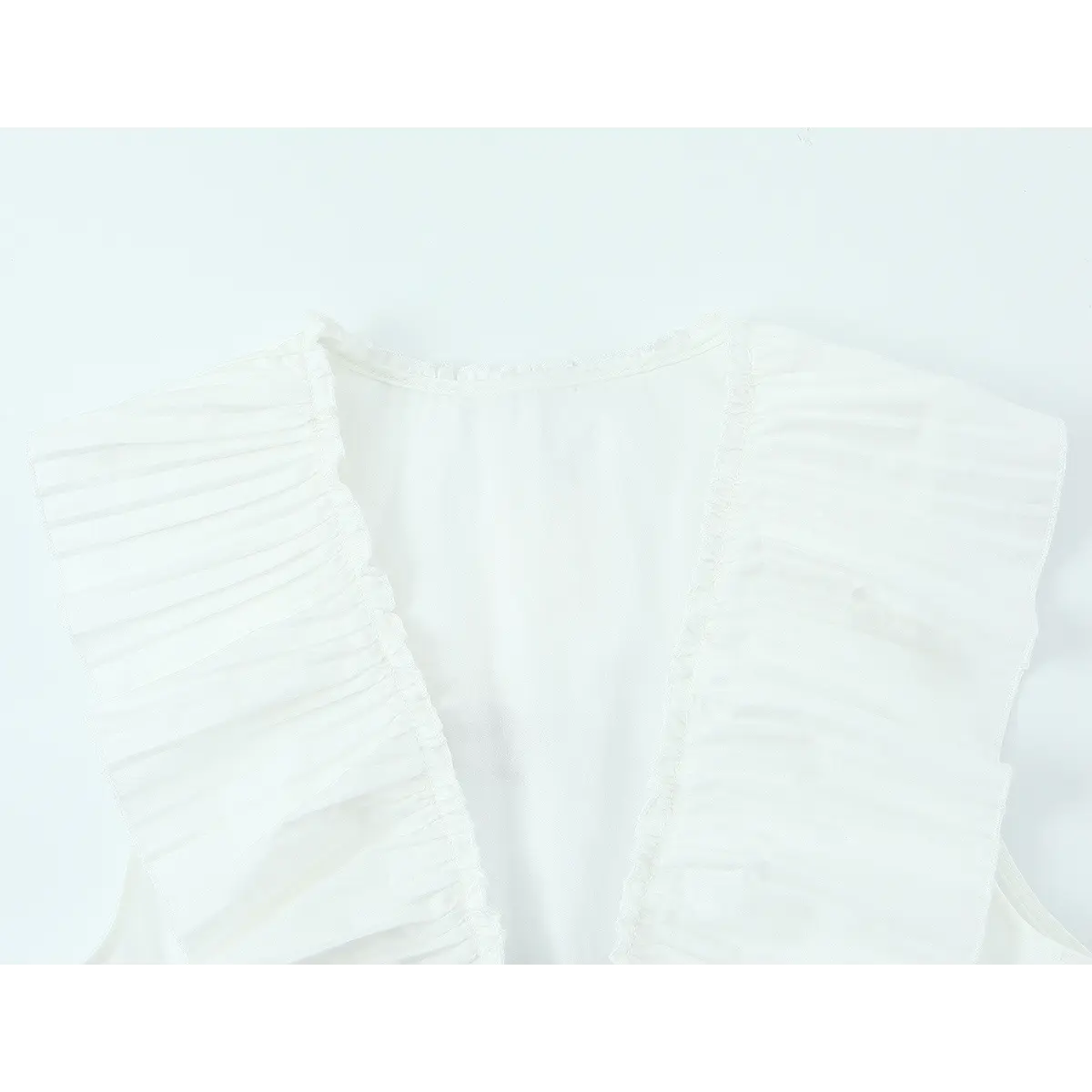 Front view of the white ruffle top, showing the pleated wing sleeves, V-neckline, and gathered neck trim