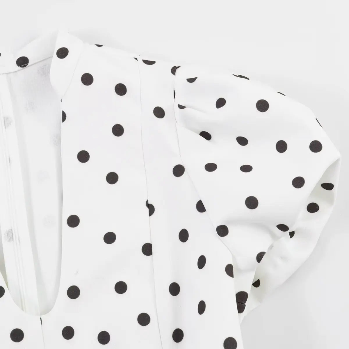 Close-up of the V-neckline, standing collar, and puffed short sleeve on the white polka dot dress.