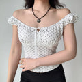 Woman wearing a white polka dot puff sleeve top styled off-the-shoulder, paired with a black skirt and flower necklace.