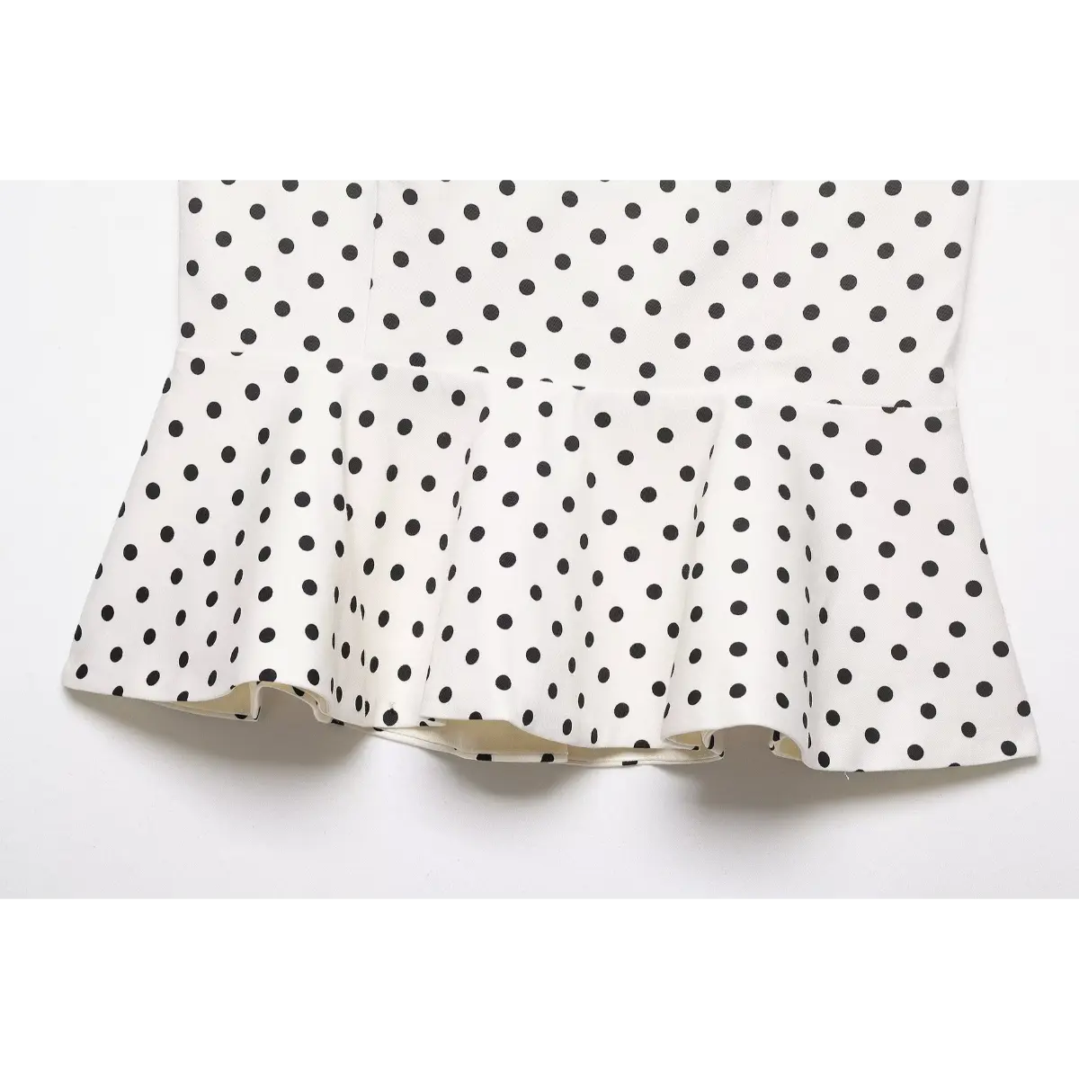 Close-up of the flared peplum hem on the white polka dot strapless top