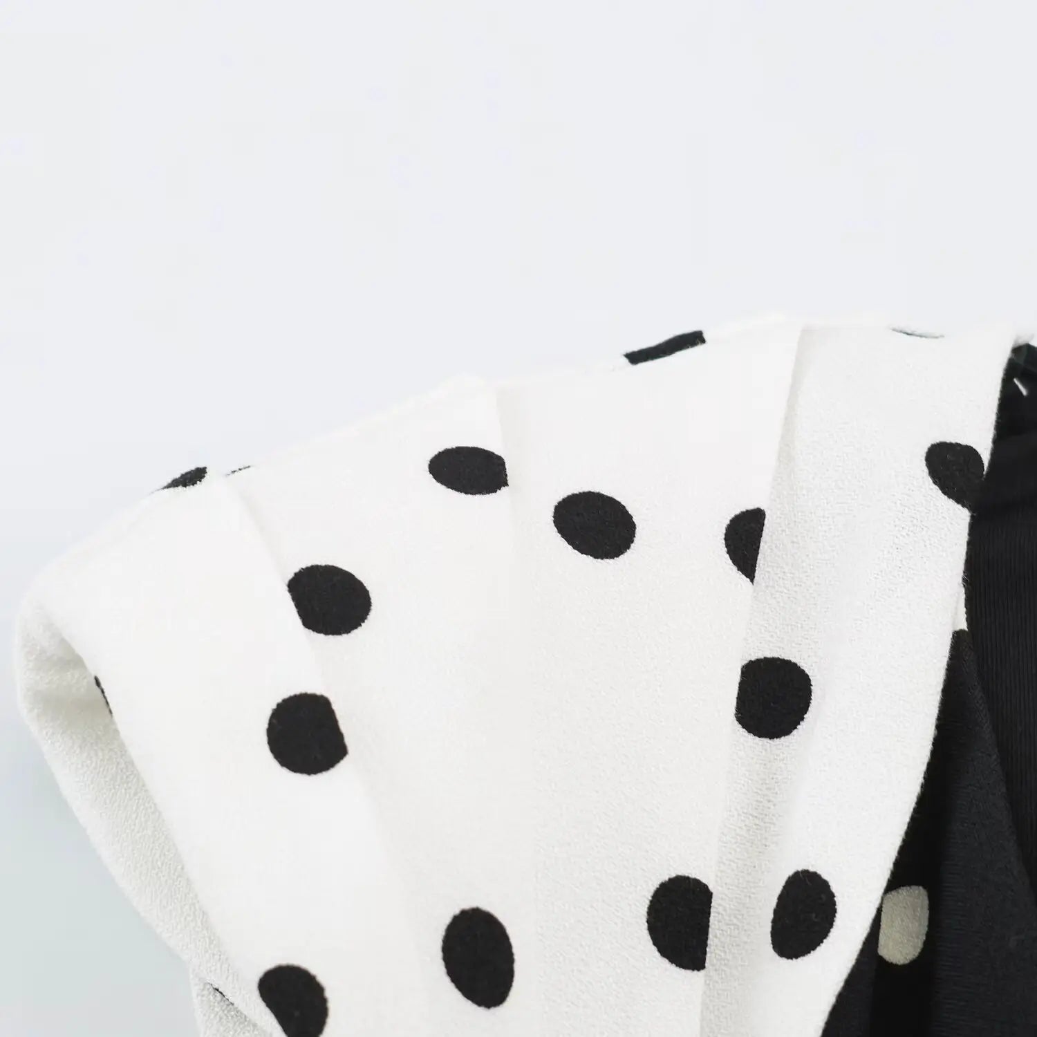 Close‑up texture of white fabric with black polka dots pleated cap sleeve