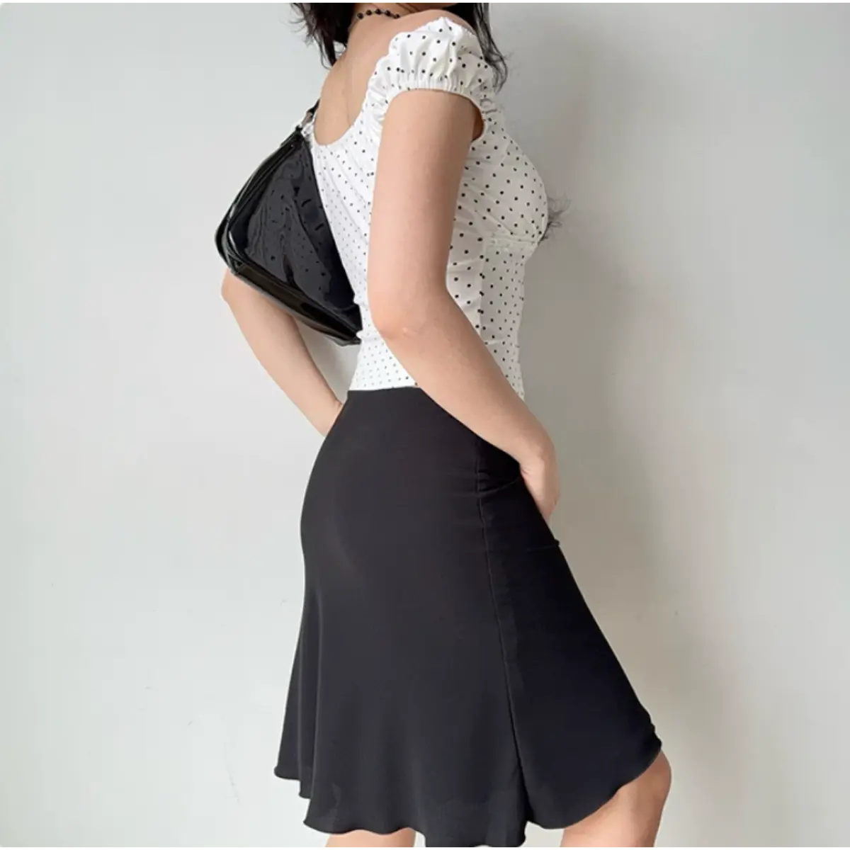  Woman in a white polka dot puff sleeve top, styled with a black midi skirt and a black handbag, shown from the back.
