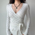 Front torso shot white polka dot wrap v‑neck long sleeve top with side waist tie knot fitted silhouette