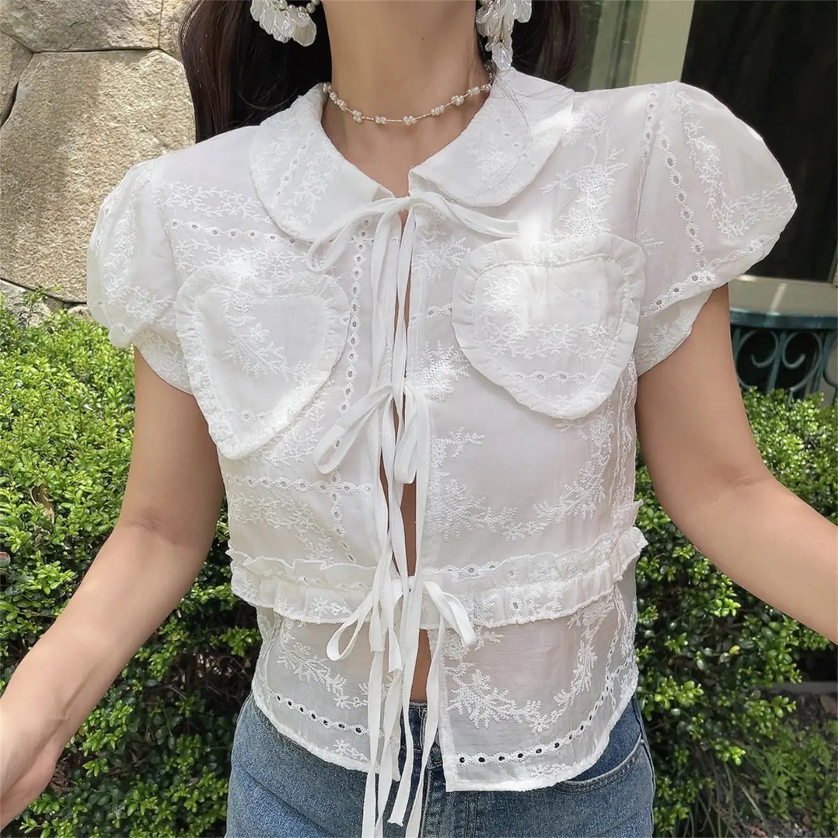 Slight angle view of the white embroidered puff-sleeve blouse, showing the silhouette and eyelet details.
