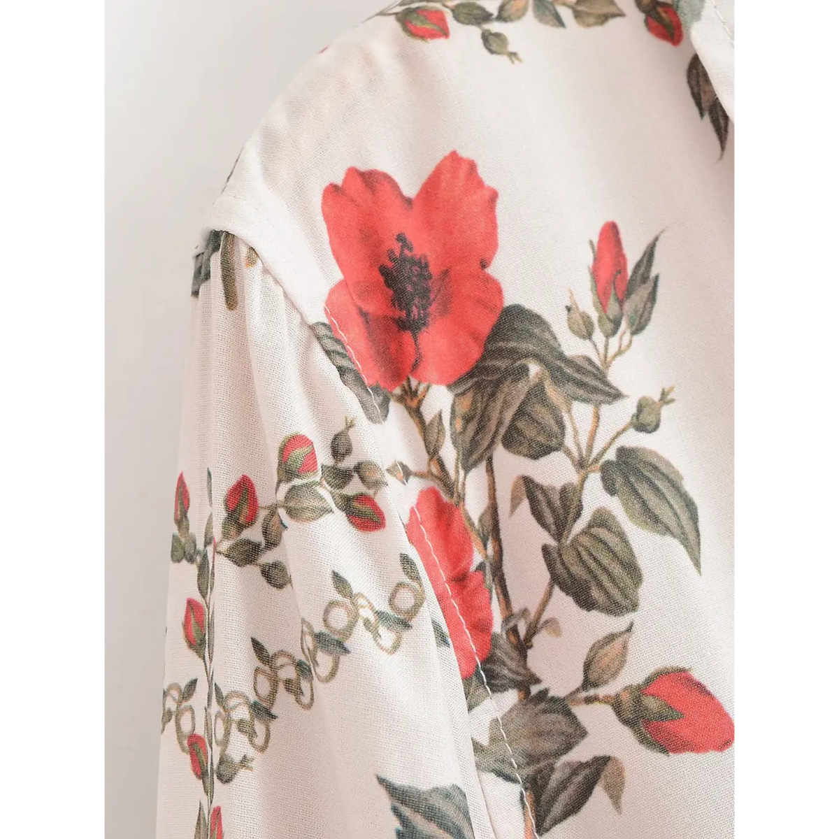 Shoulder detail of white maxi dress with large red flower motifs, green foliage and textured woven fabric