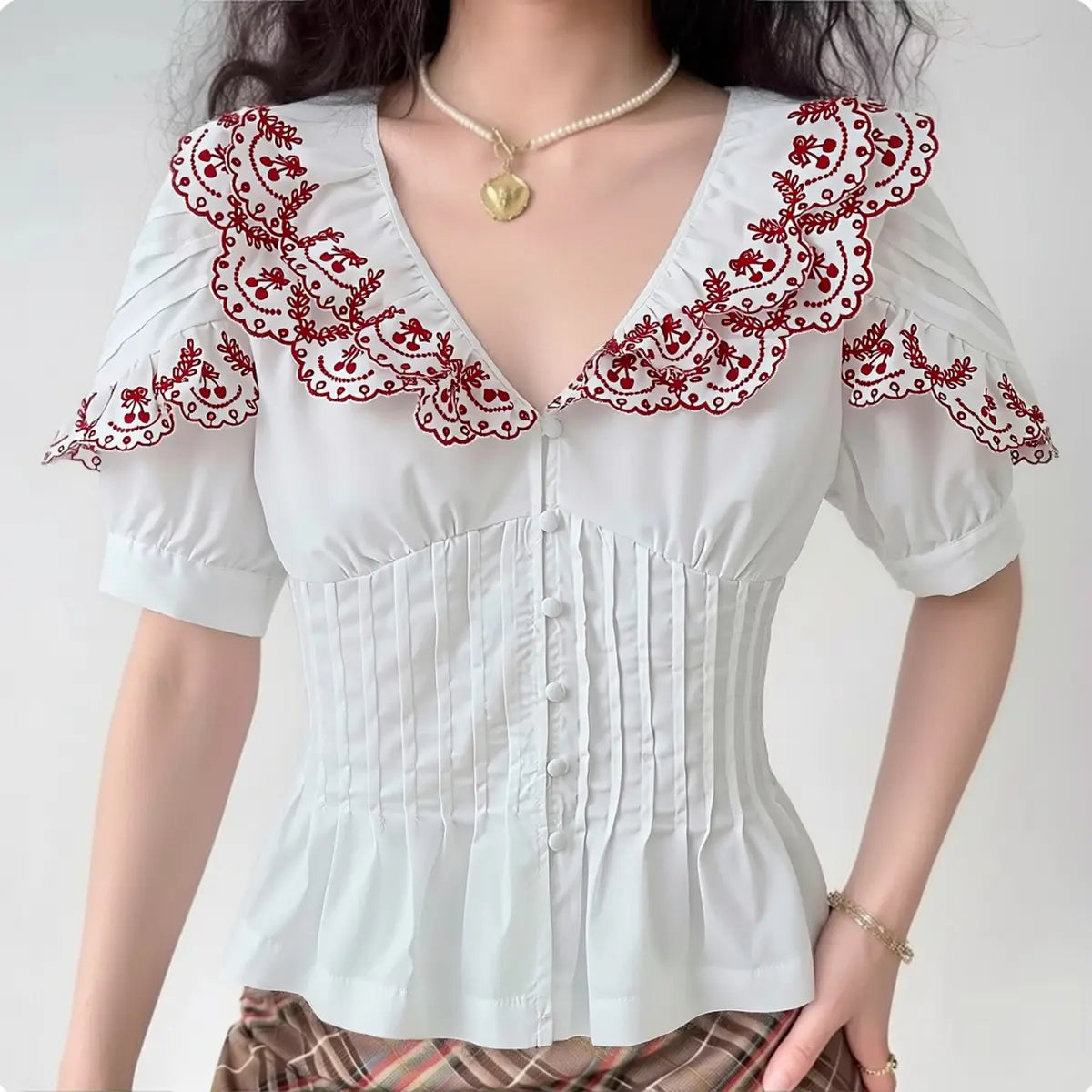 The blouse styled on a model, showcasing the red embroidered collar details, fitted pleated waist, and pairing with plaid bottoms.