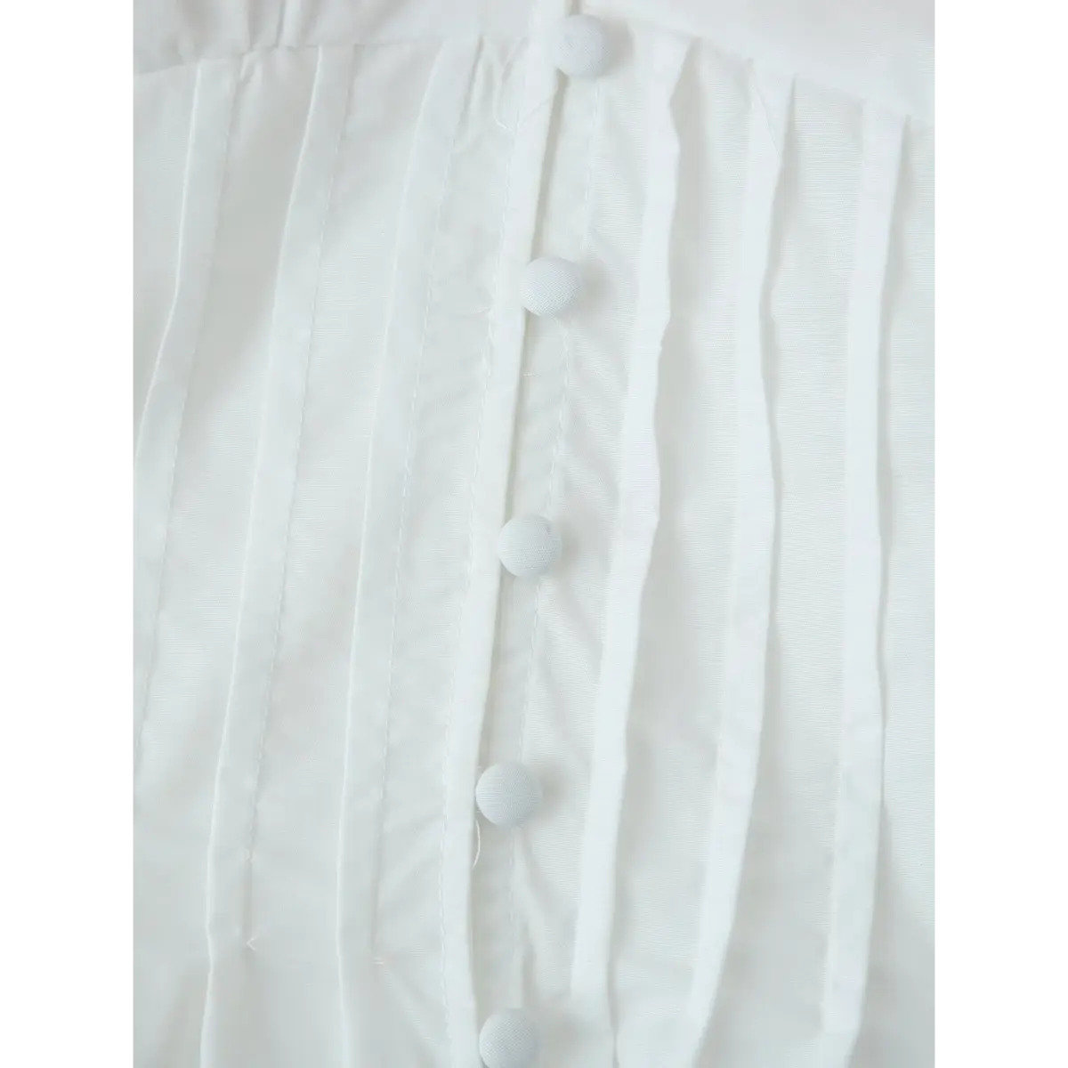 Close-up of the blouse's front placket, showing the round buttons and sharp vertical pleats.