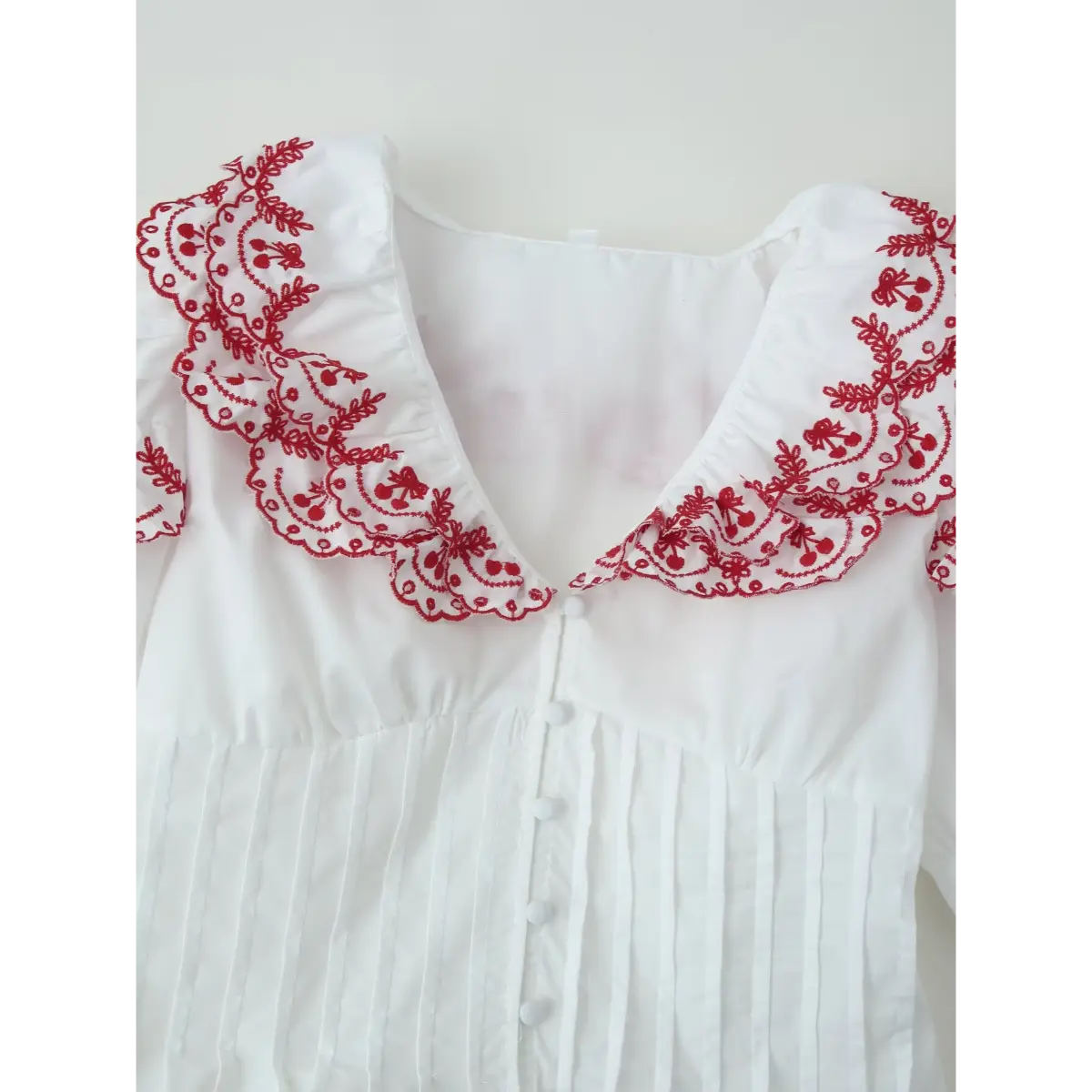 Front view of the blouse's neckline, highlighting the V-shaped red embroidered ruffled collar and button placket.