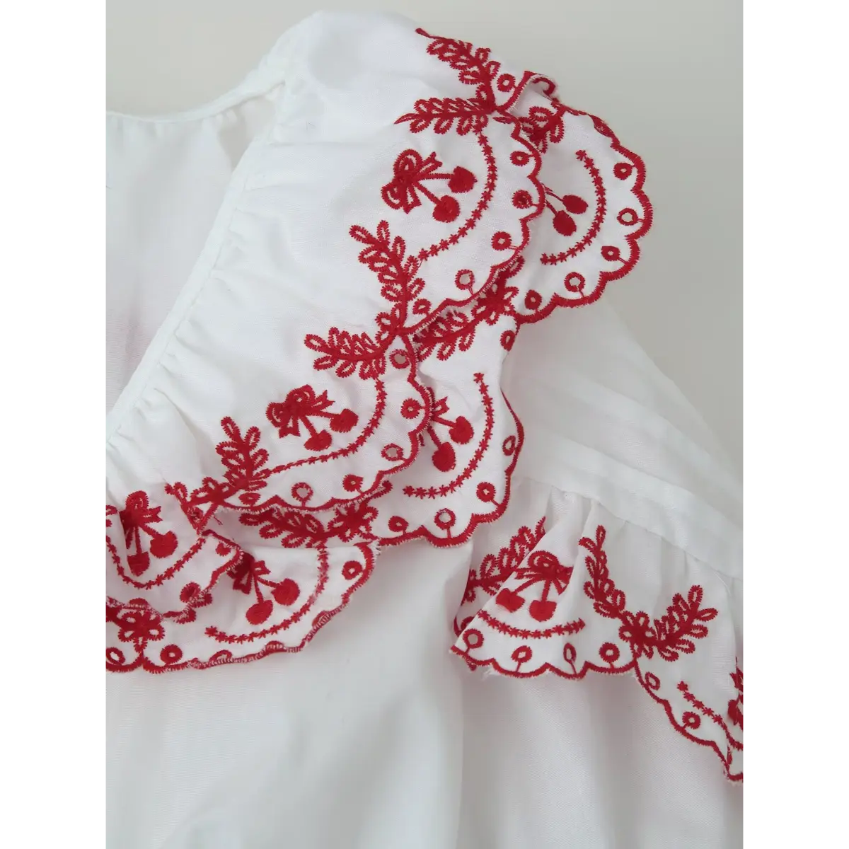 Close-up of the blouse's collar and sleeve, showcasing the double-layered red cherry embroidery on the scalloped ruffles.