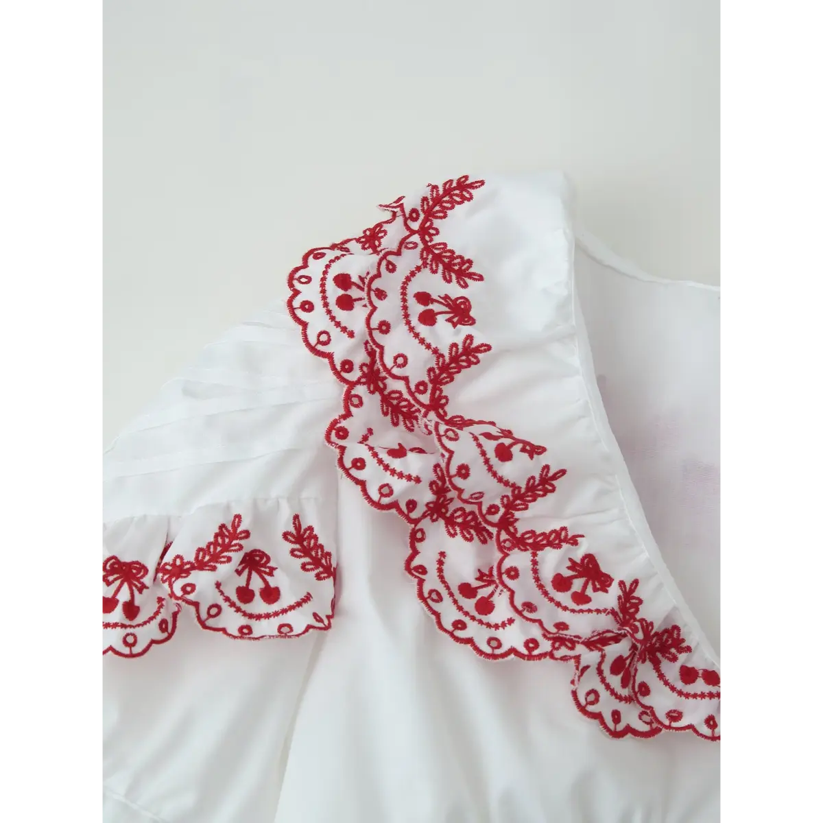 Close-up of the blouse's ruffled collar, showcasing the intricate red cherry and leaf embroidery.