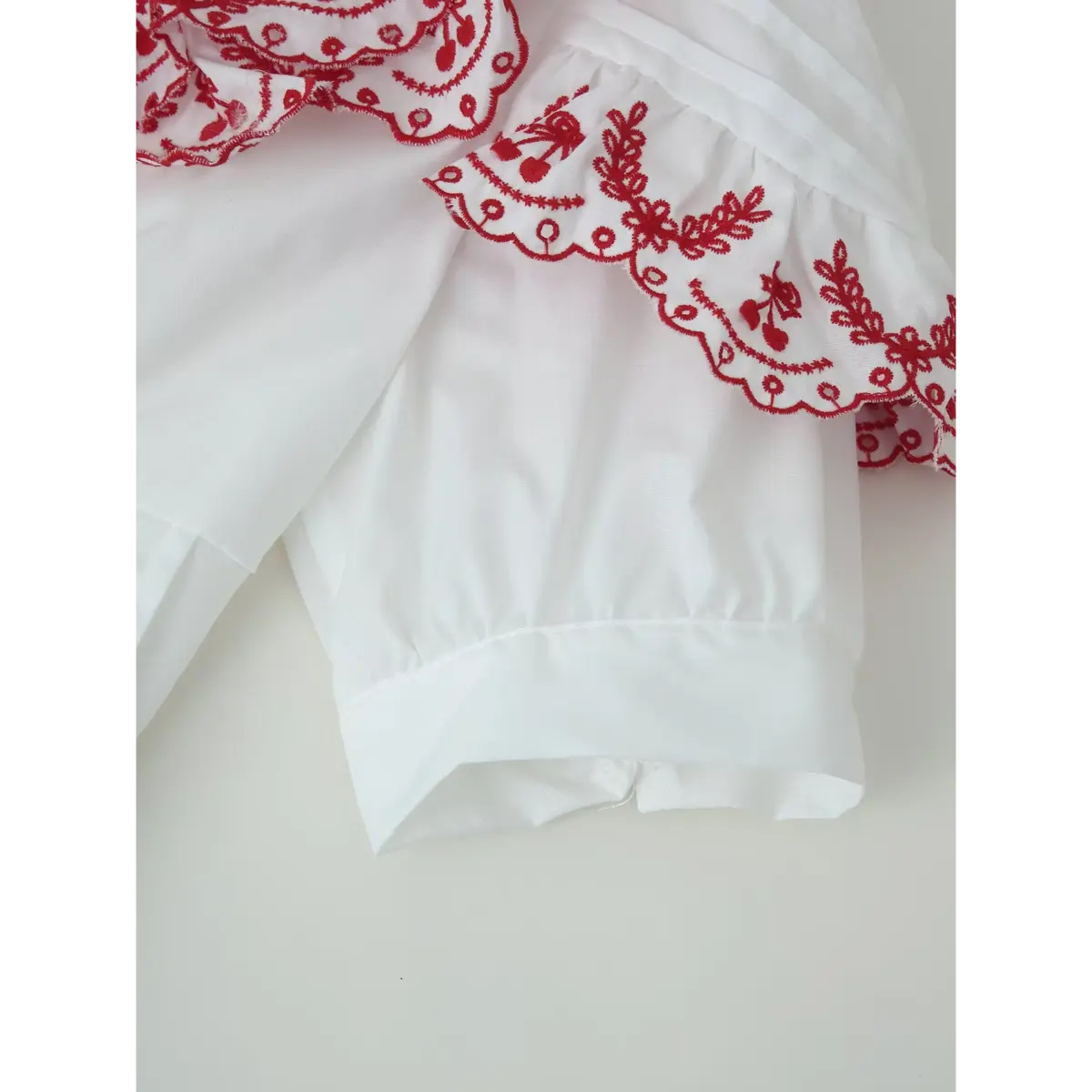  Close-up of the blouse's puffed sleeve and cuff, showing the red embroidered ruffle and neat hem.