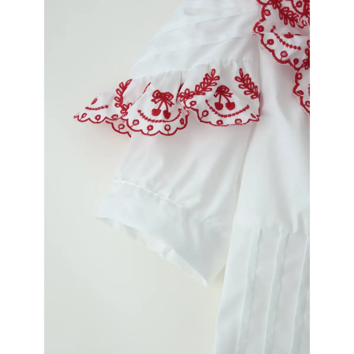 Close-up of the blouse's puffed sleeve, featuring the red embroidered ruffled cuff and clean seam.