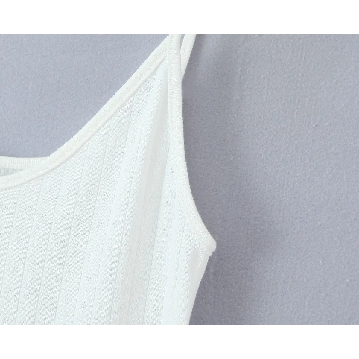 Close-up of the thin spaghetti strap and scoop neckline, showing the vertical ribbed texture and eyelet knit pattern.