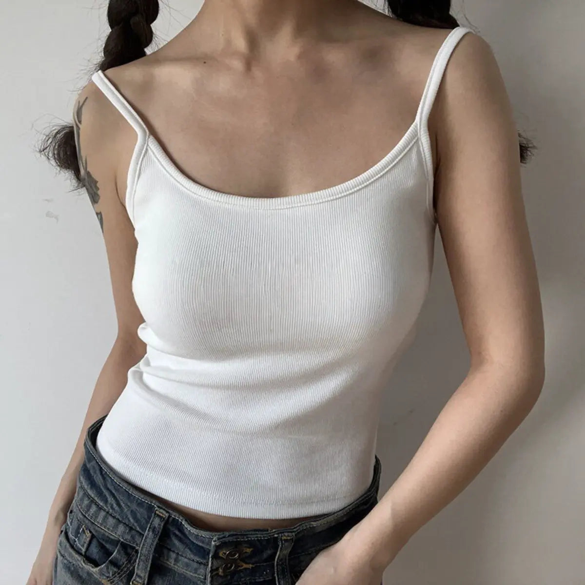 Lifestyle shot of form-fitting white ribbed camisole with thin straps, tucked into jeans