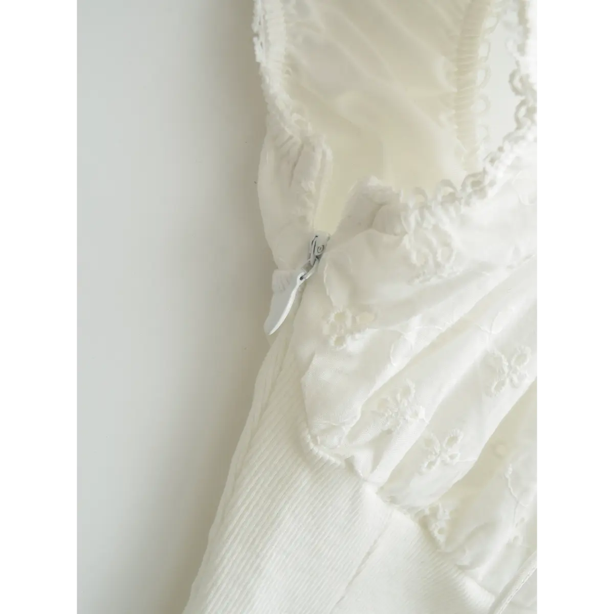 Close-up detail of white embroidered ribbed top, focusing on the side zipper and inner lining construction.