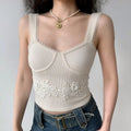 Model wearing a white ribbed cami top with bustier-style seams, scalloped straps, and a floral lace waistband, paired with jeans.