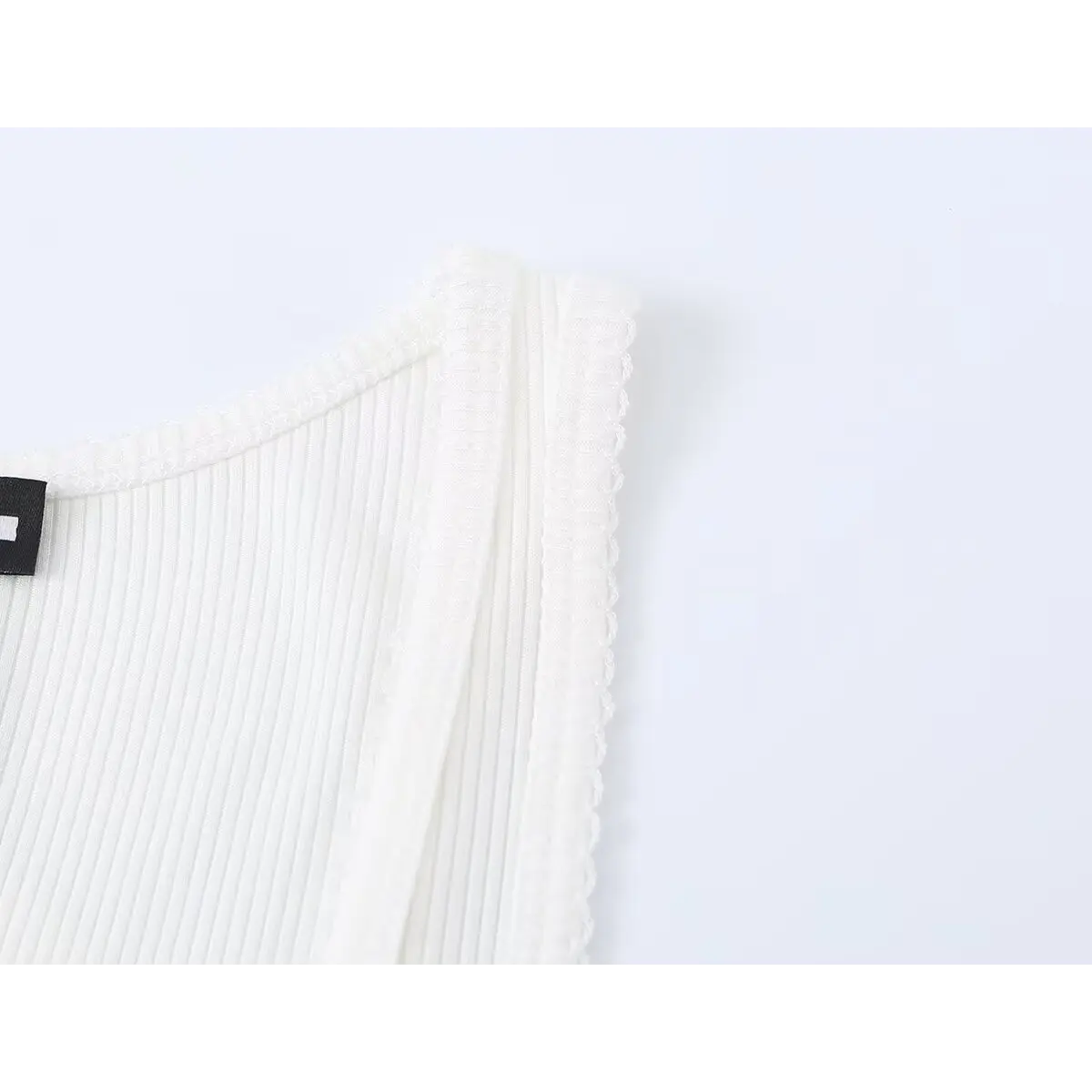 Close-up of the scoop neckline and inner brand label on the white ribbed tank top