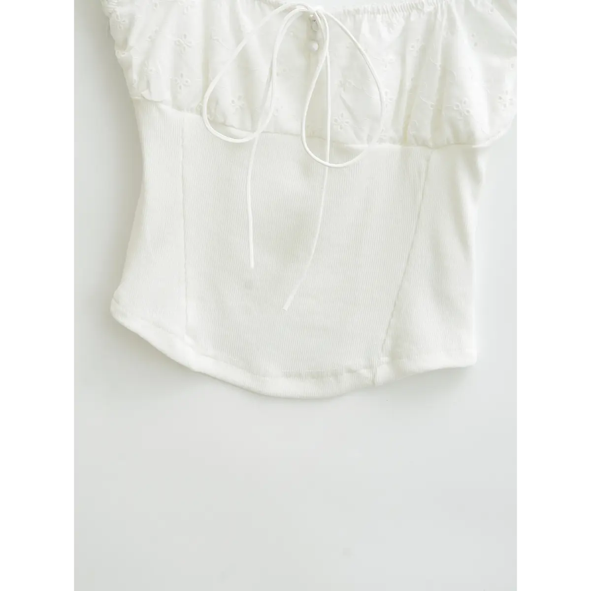 Close-up of the ribbed bodice on white embroidered top, showing panel stitching and curved hem design.
