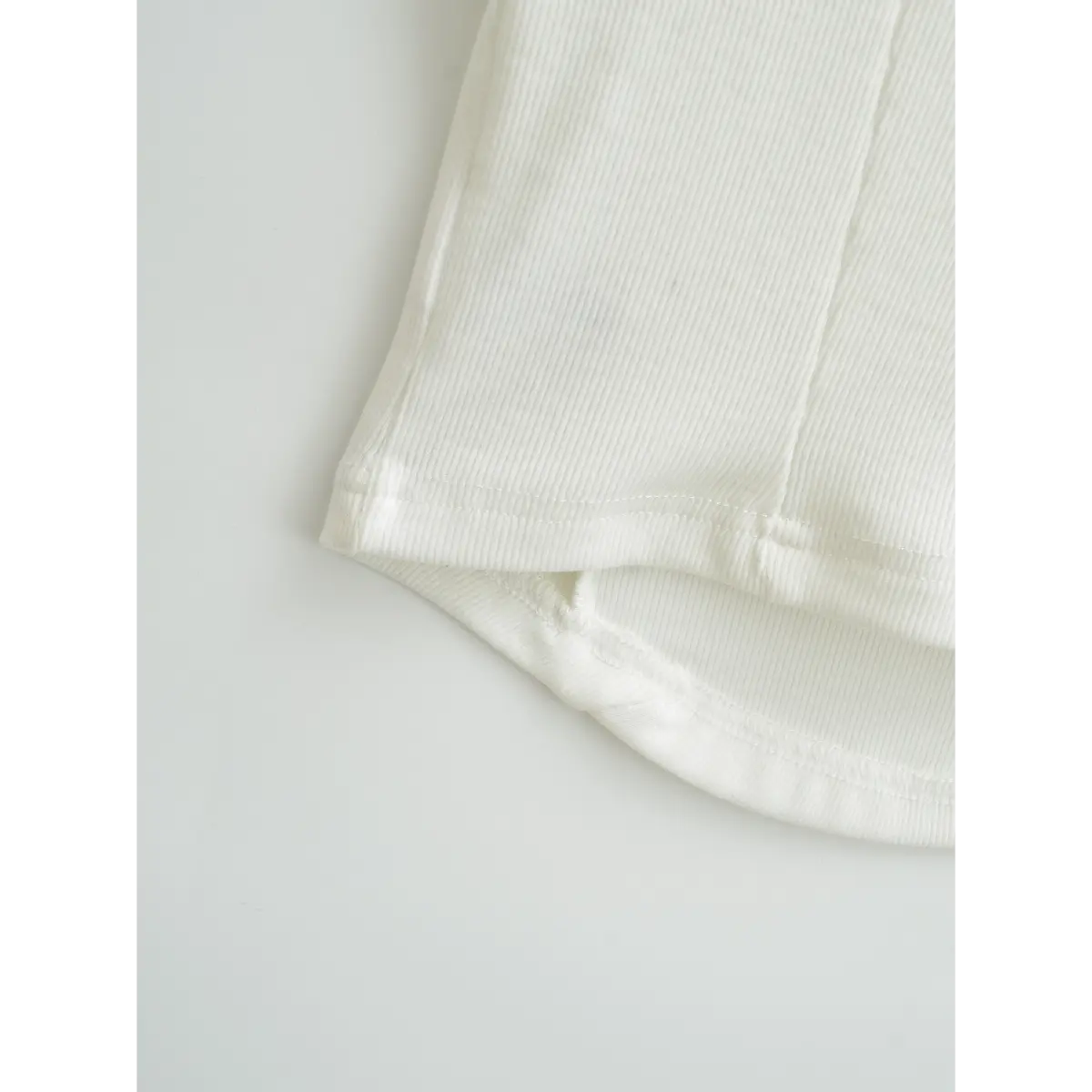 Close-up of the hem of white ribbed top, showing curved bottom edge and neat stitching finish.