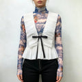 Model wearing white ruched peplum vest with front black tie bow, layered over blue cloud angel print mesh turtleneck top
