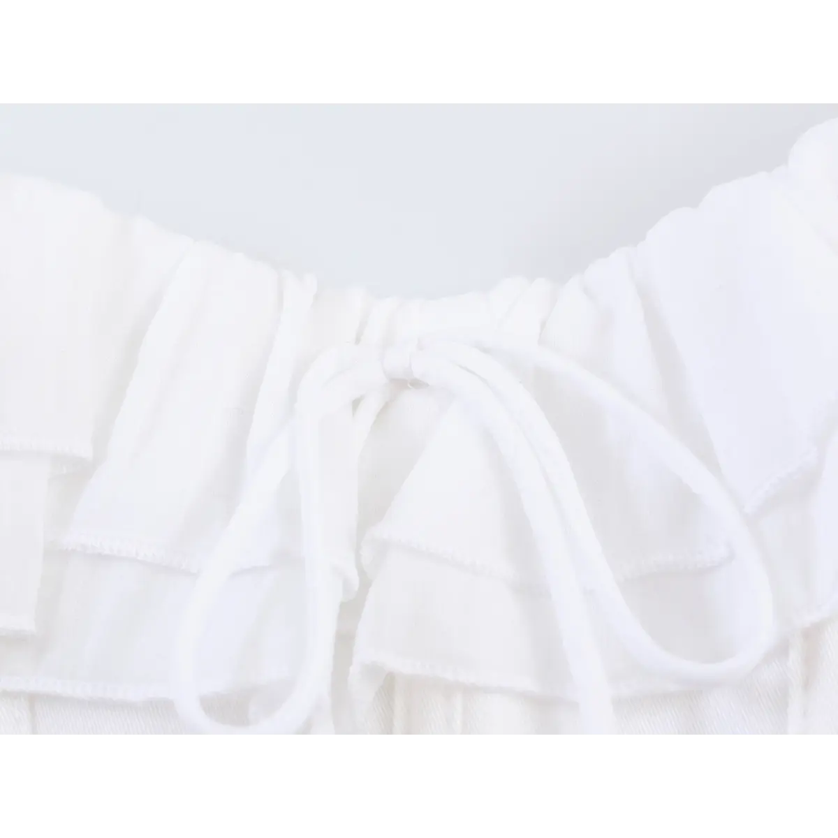 Close-up of the front tie bow detail on the white ruffled corset-style cami