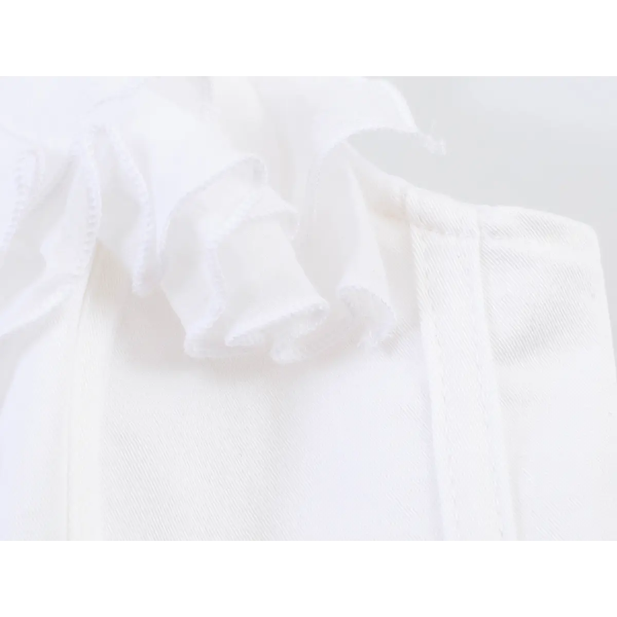 Close-up of the lightweight fabric texture and ruffled detailing on the white cami top