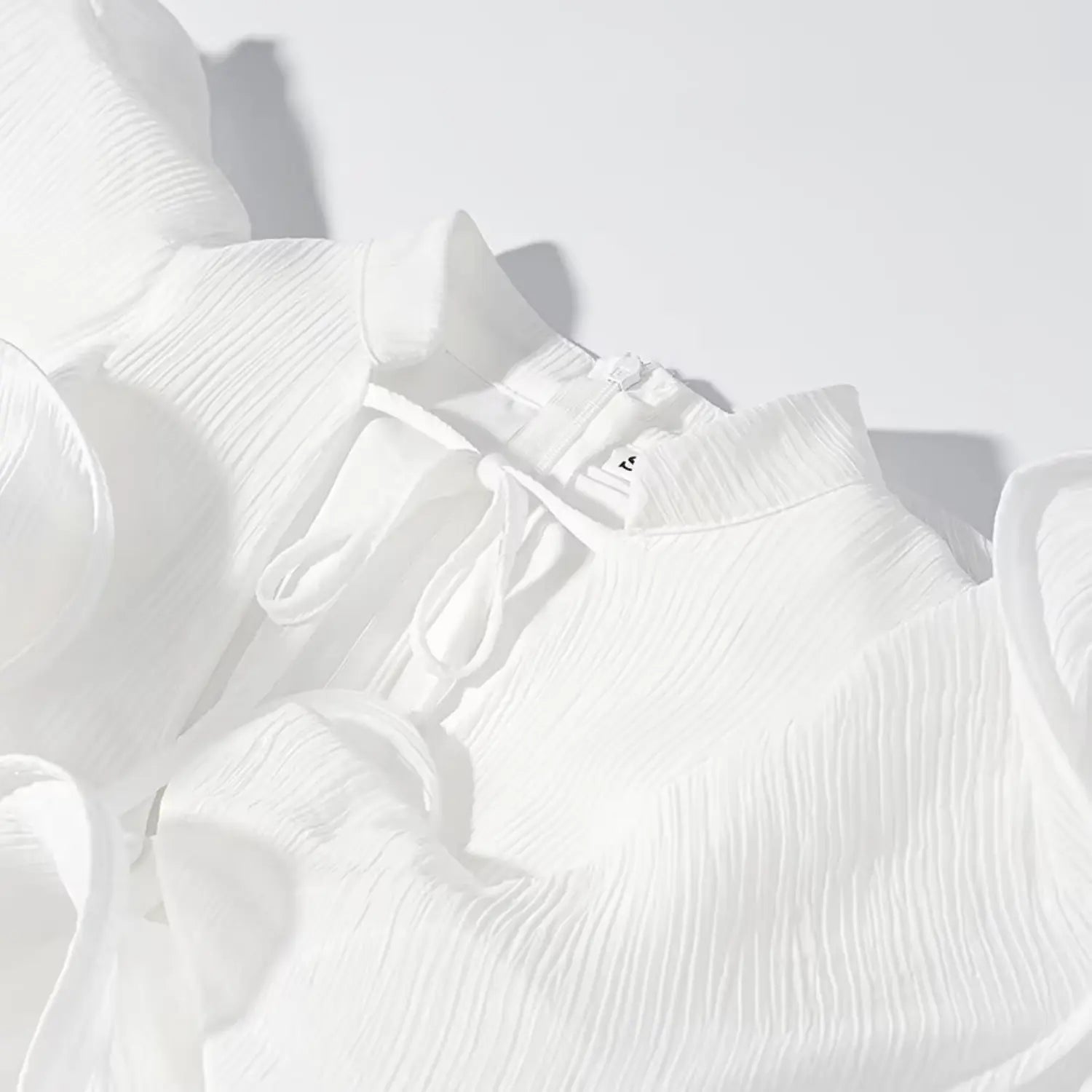 Close-up detail of dress stand collar, front tie string and invisible back zipper on white textured fabric