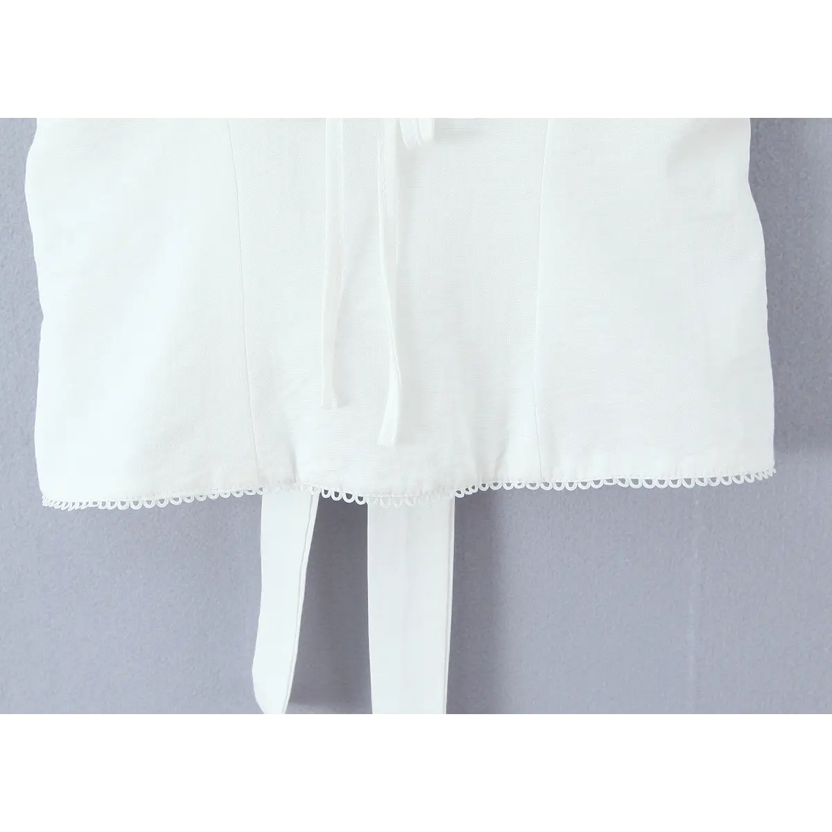 Close-up of the scalloped hem and waist tie detail on the white camisole.