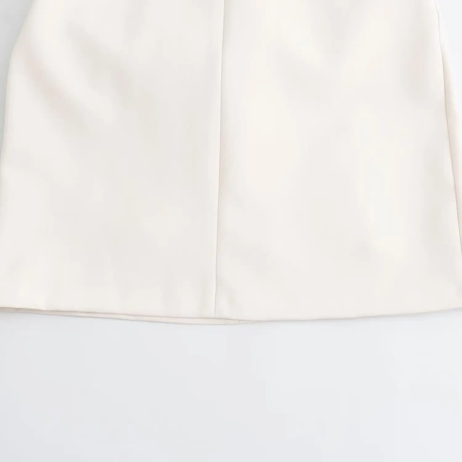 Flat‑lay close‑up of neat finished hem and center seam on white fitted sheath mini dress