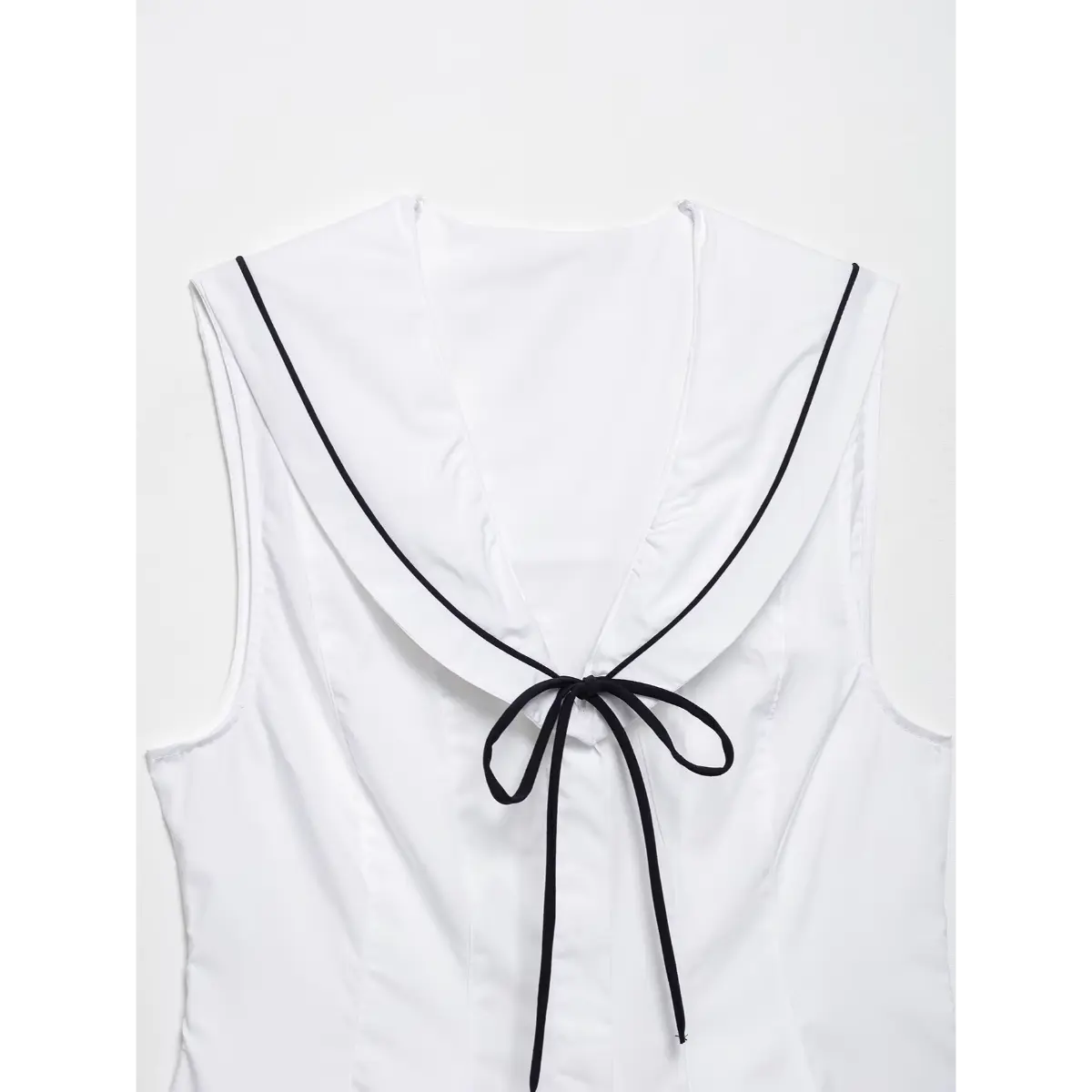 Close-up of the black contrast tie and neckline trim on the white top.