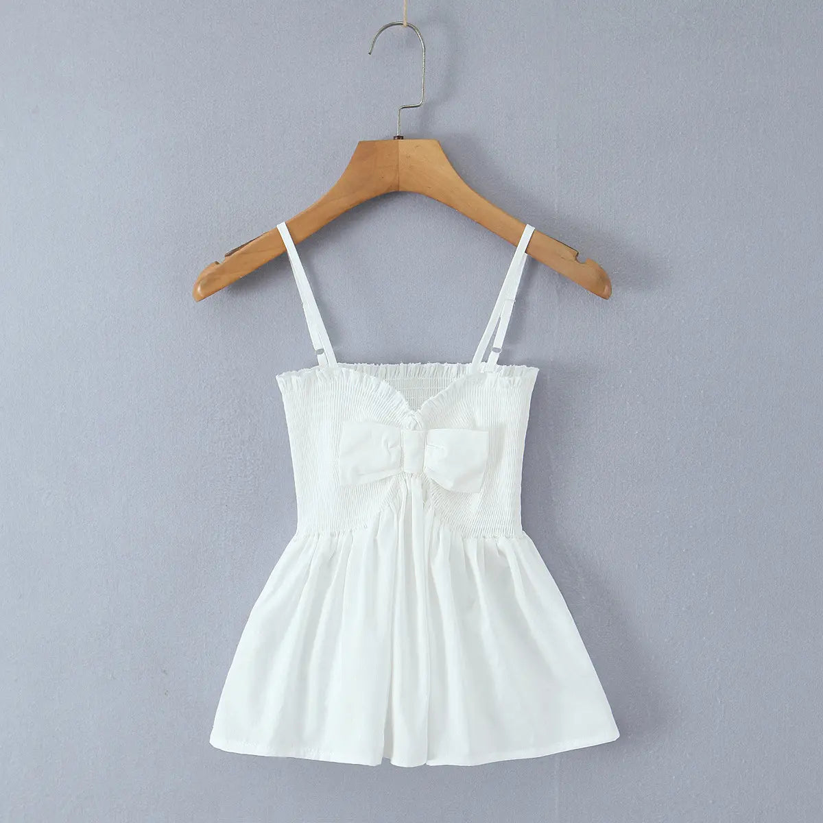 Full front view of white cami top with smocked bust, center bow and flared peplum hem.