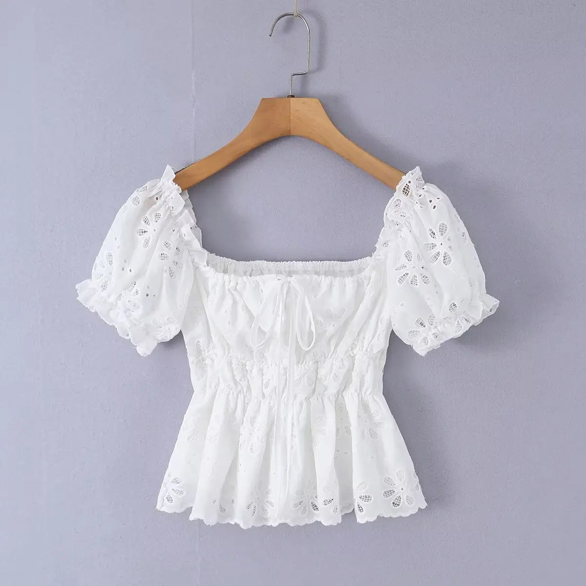 White eyelet embroidered top hanging on wooden hanger, front view