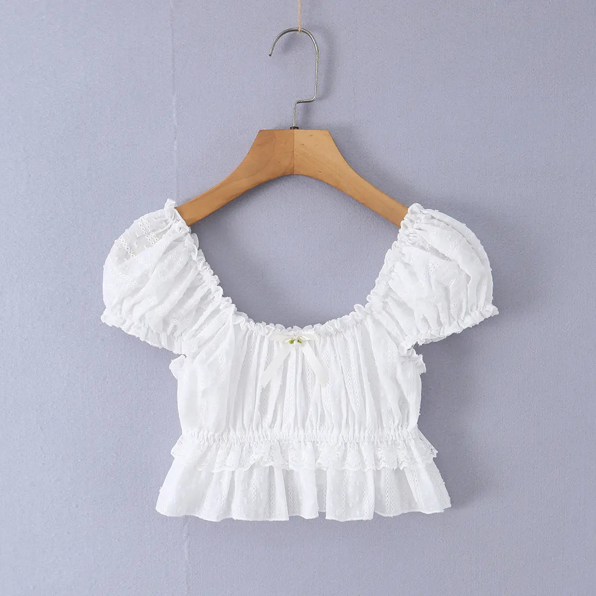 Full front view of the white top, featuring a square neckline, puff sleeves, front bow detail, and ruffled peplum hem.