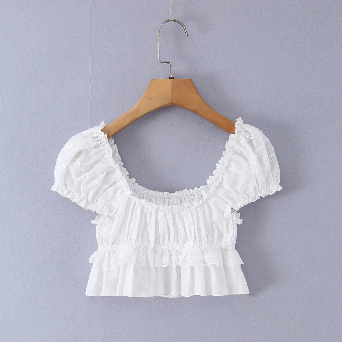 Full view of the white lace top, displaying the square neck, puff sleeves, gathered bodice, and ruffled peplum hem.