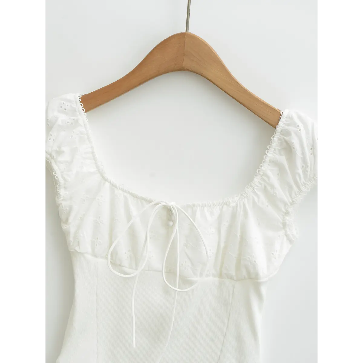 Close-up of the square neckline on white embroidered top, showing lace trim, puff sleeves and gathered fabric.