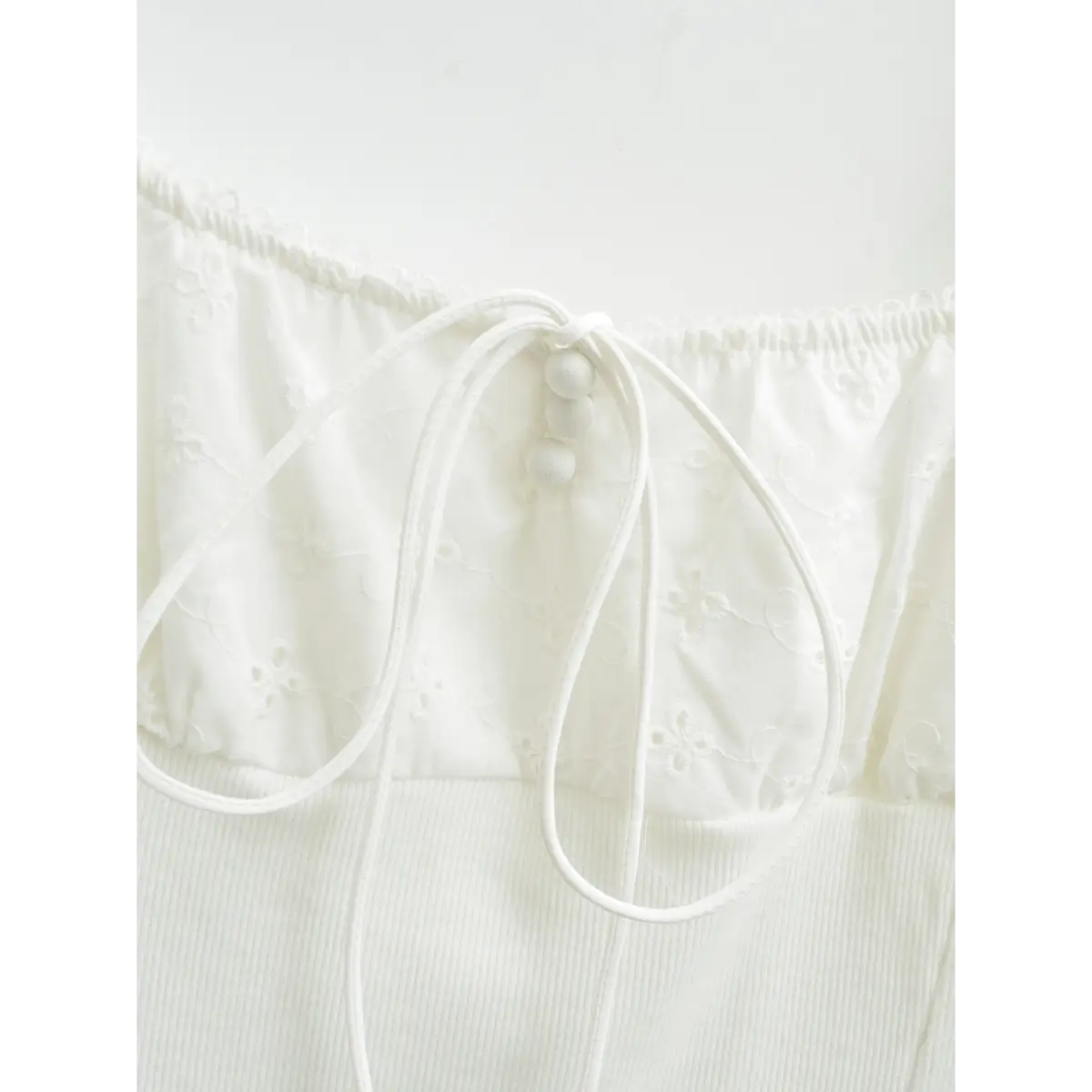 Close-up view of the tie detail on white square-neck top, with drawstring and decorative buttons.