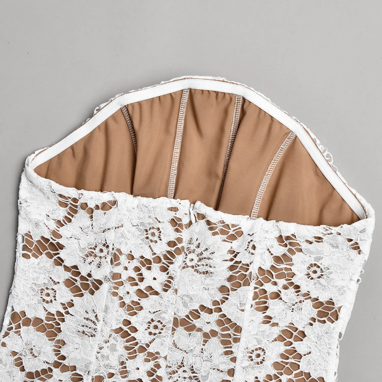 Close‑up shot inner boning and nude lining construction of white strapless lace dress bodice
