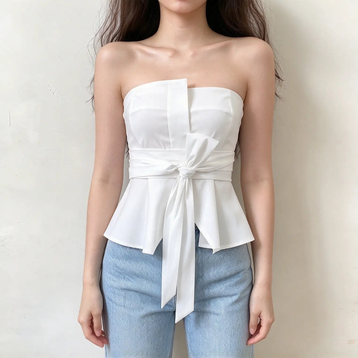 Model wearing white strapless tie waist peplum top with jeans, front view
