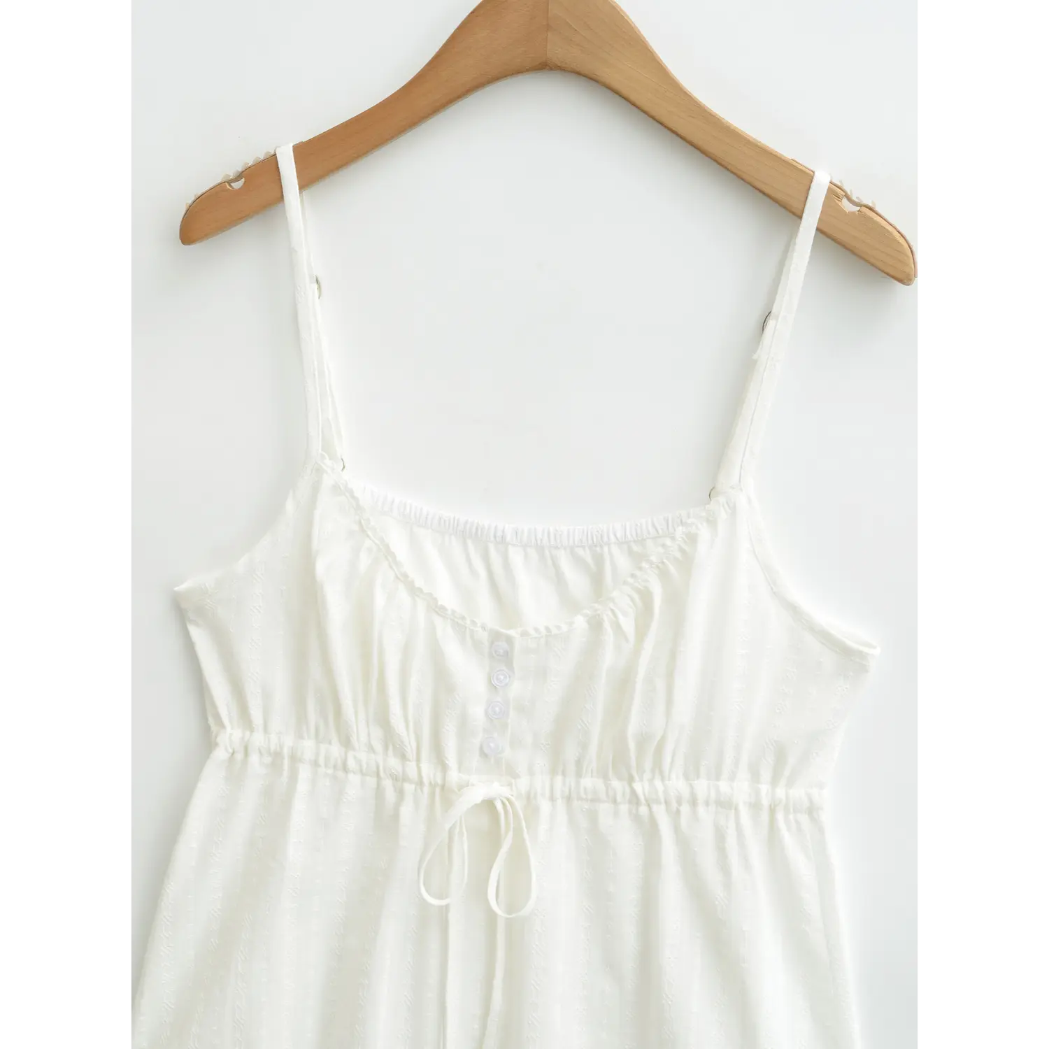 Close-up of the bust area on a white textured camisole top, showing the button placket and drawstring