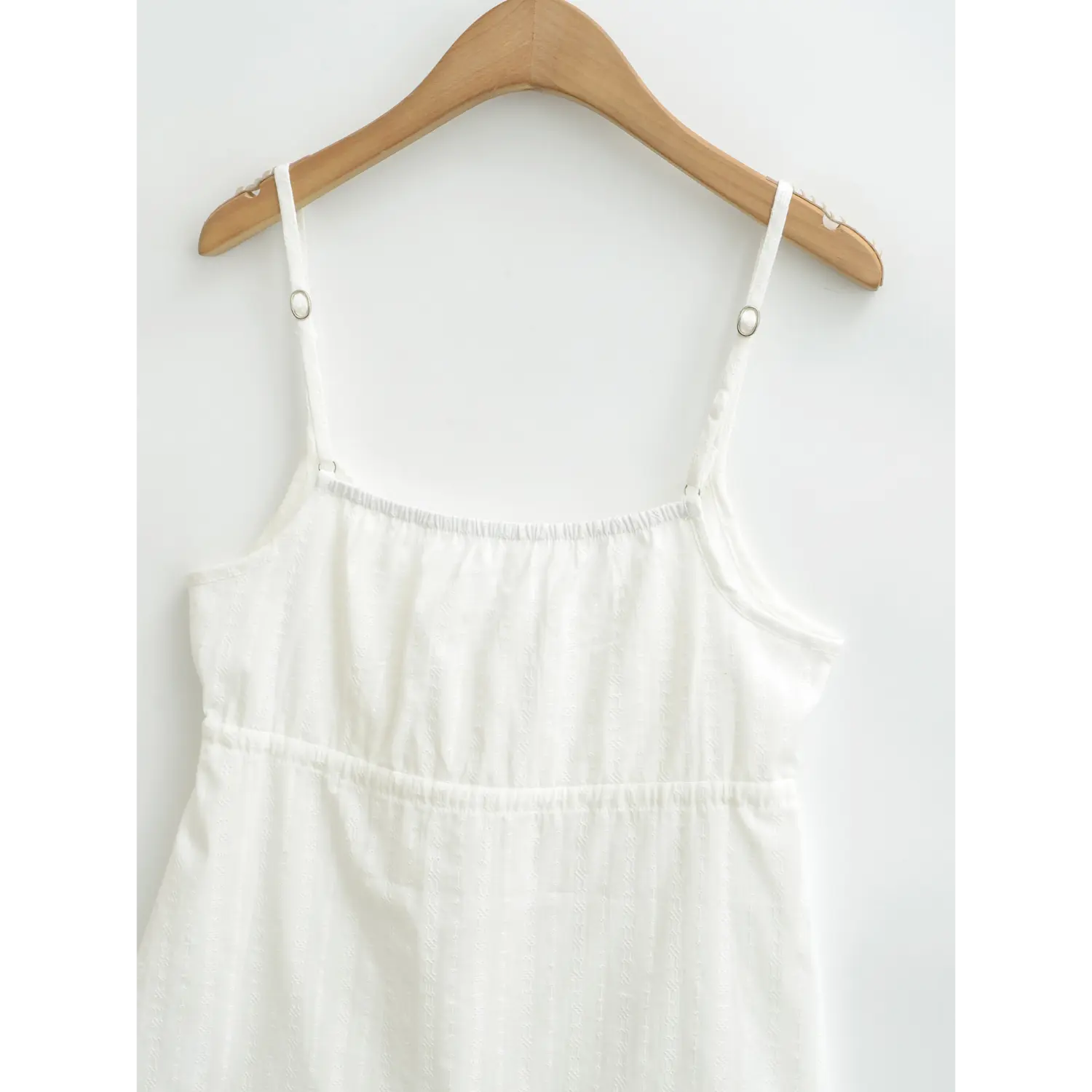 Close-up of the front of a white textured camisole top, showing the neckline and adjustable straps