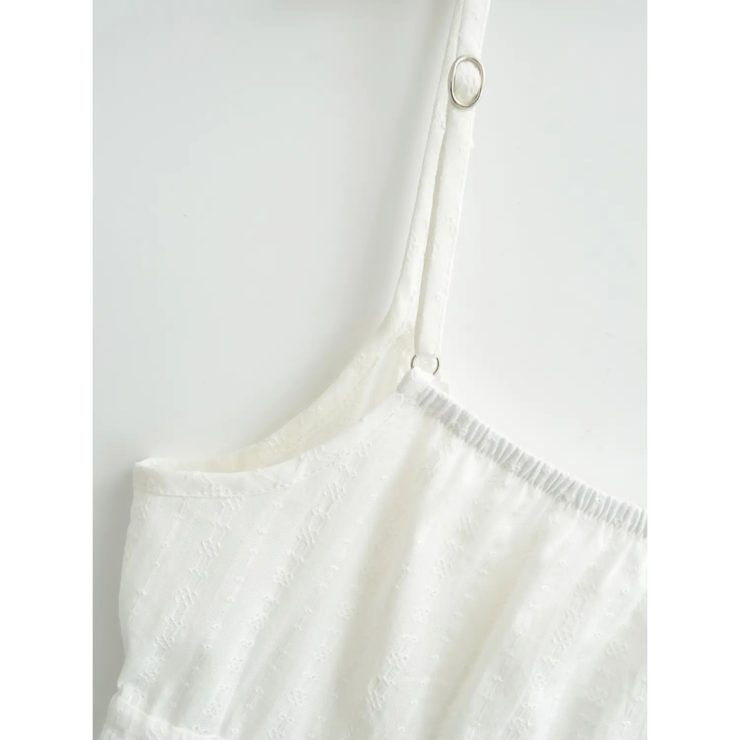 Close-up of the adjustable strap slider on a white textured camisole top