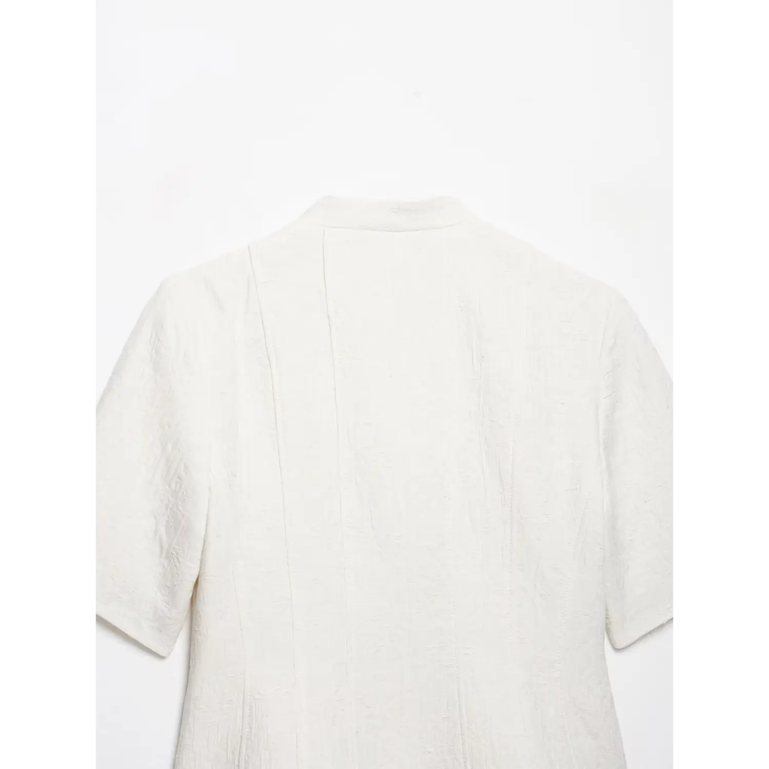 Full flat‑lay back view of white textured cropped short sleeve jacket, stand collar, vertical tailored seams, embossed jacquard fabric, white background