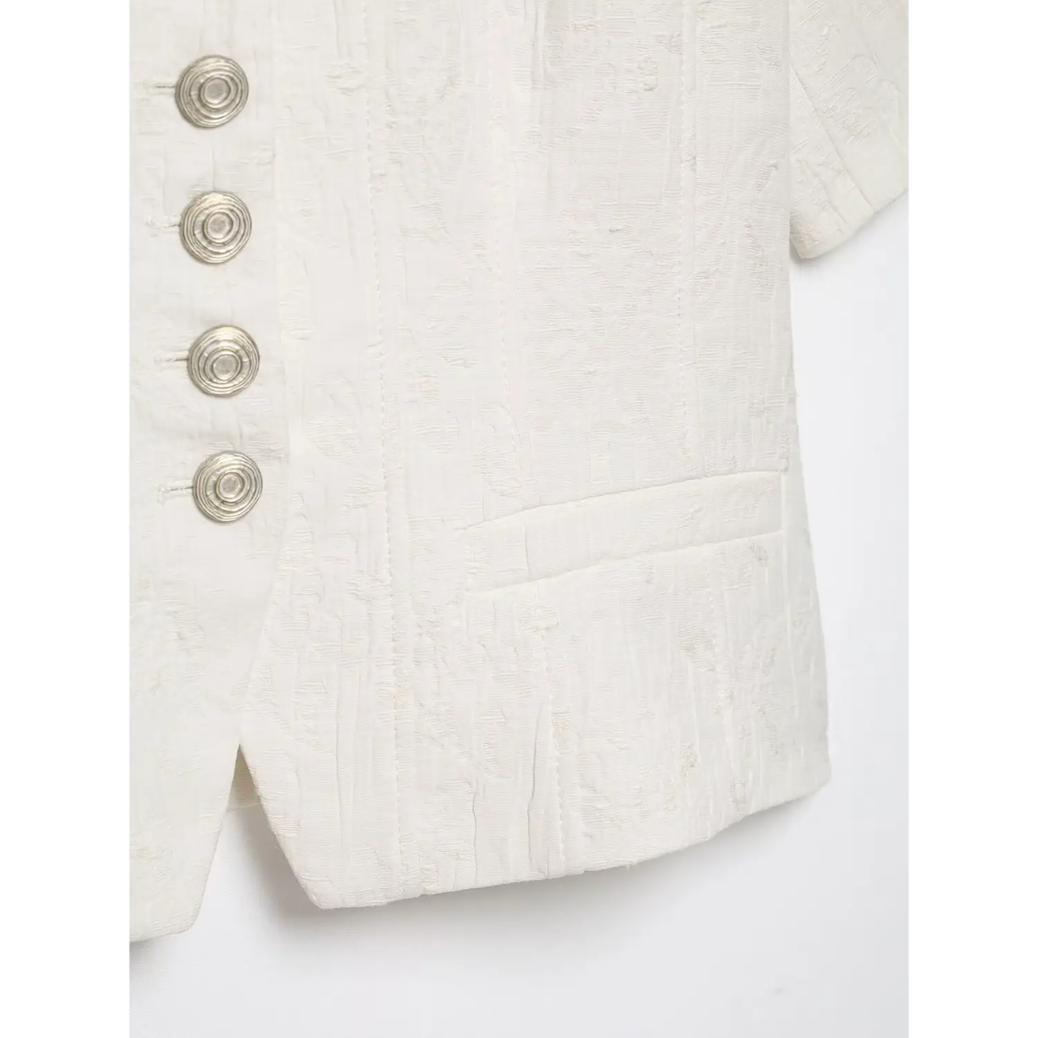 Close‑up view of front patch pocket, silver spiral buttons and hem stitching on white textured cropped short sleeve jacket, embossed jacquard fabric, white background