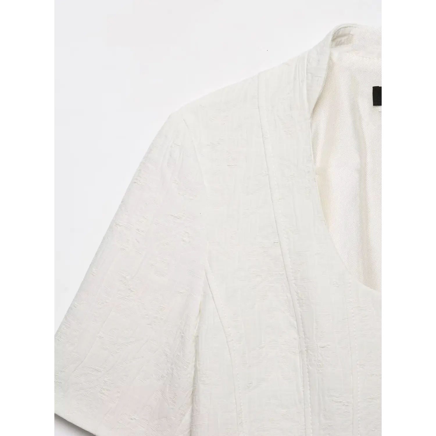 Close‑up shot showing fabric texture, shoulder and sleeve seam detail of white cropped short sleeve jacket, embossed jacquard textile, white background