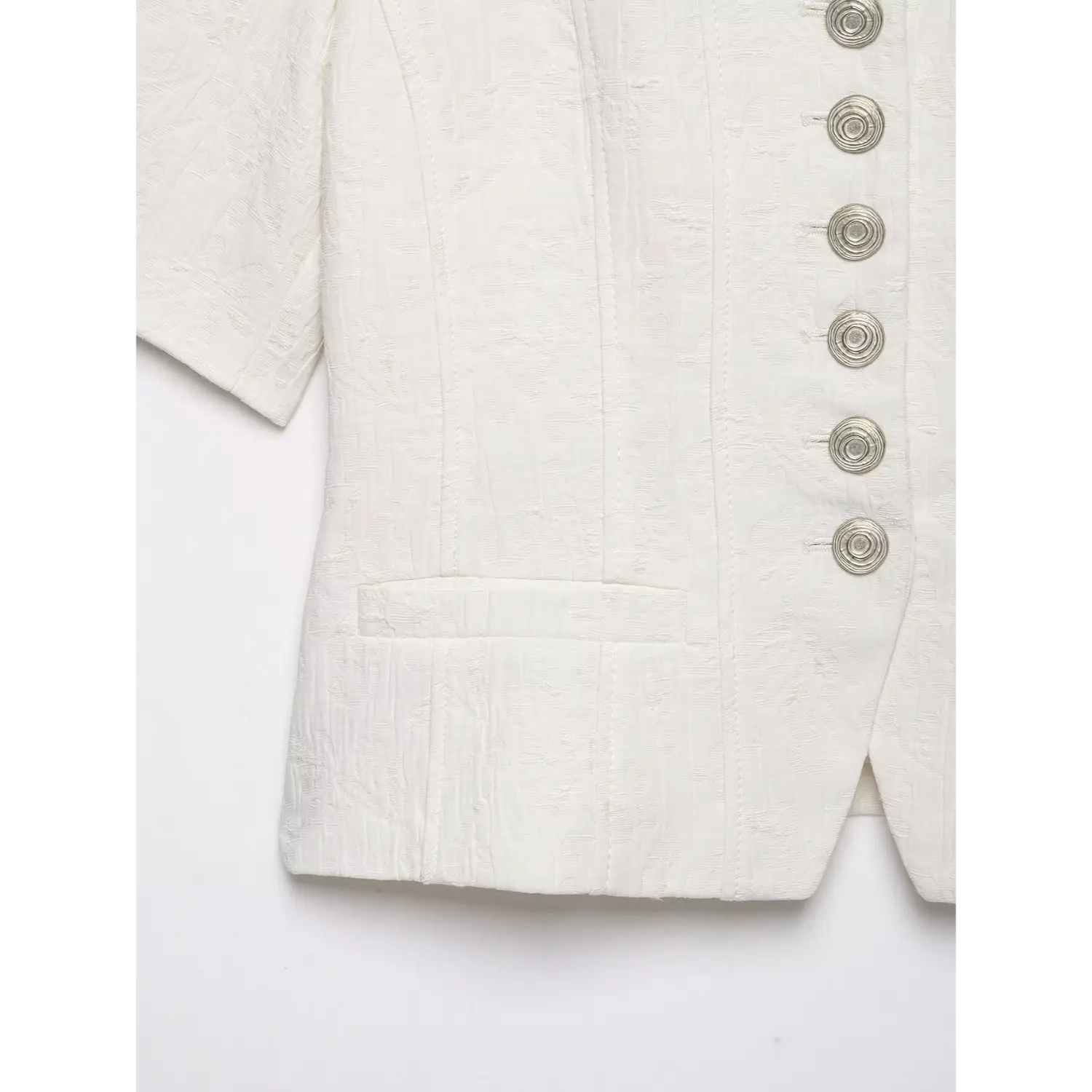 Close‑up detail of front patch pocket and hem stitching on white textured cropped short sleeve jacket, embossed fabric texture, white background