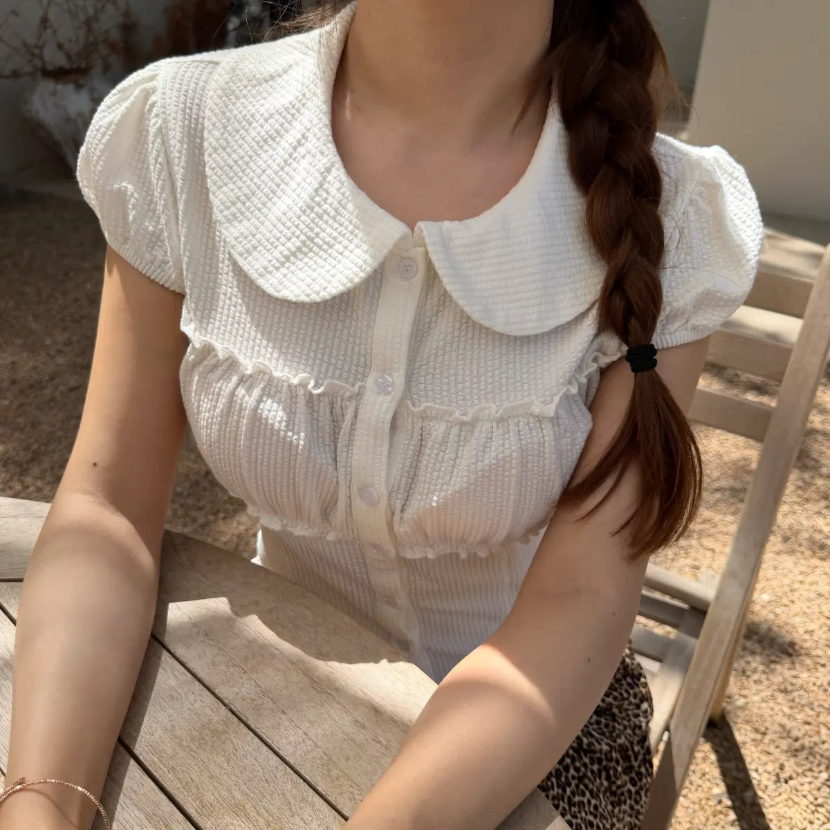 Close-up of a white textured top with a Peter Pan collar, puff sleeves, ruffled bust detailing, and front buttons.