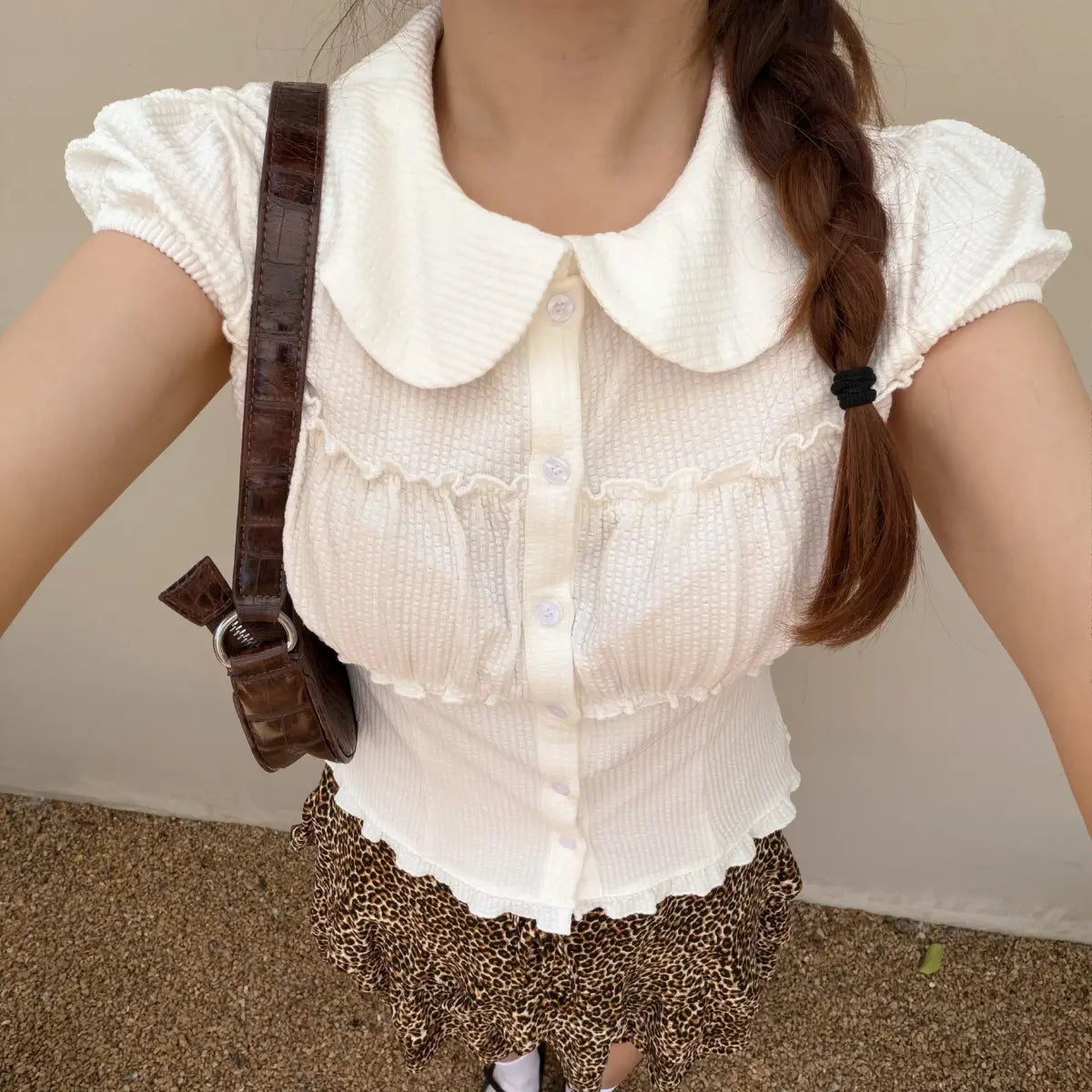 The white top paired with a brown crocodile-patterned shoulder bag, highlighting the outfit's accessories.