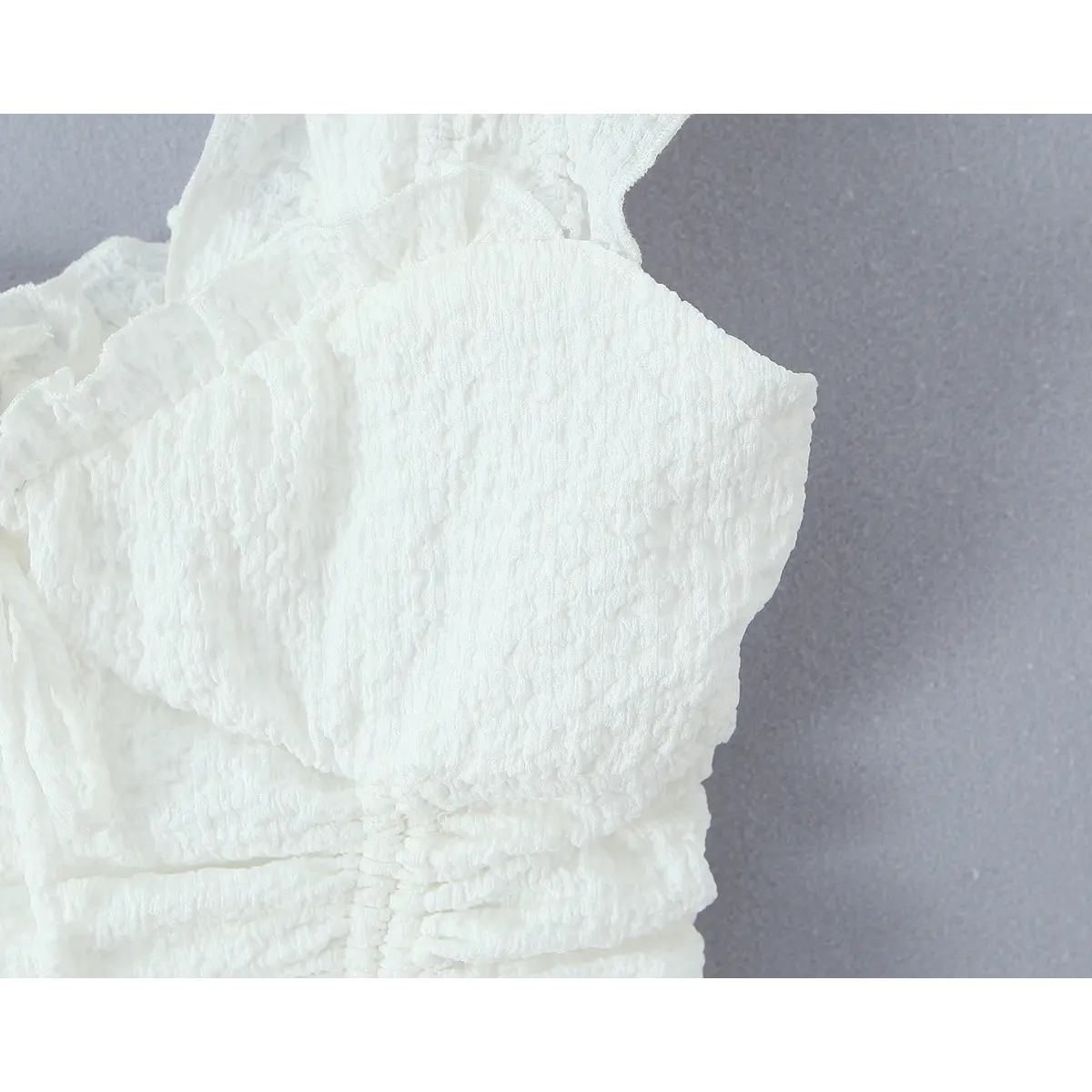Close-up of the smocked bodice and ruffled wide strap on the white tiered dress.