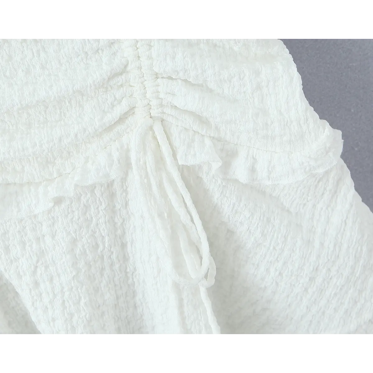Close-up of the front drawstring tie and gathered ruffle detail on the white textured dress.