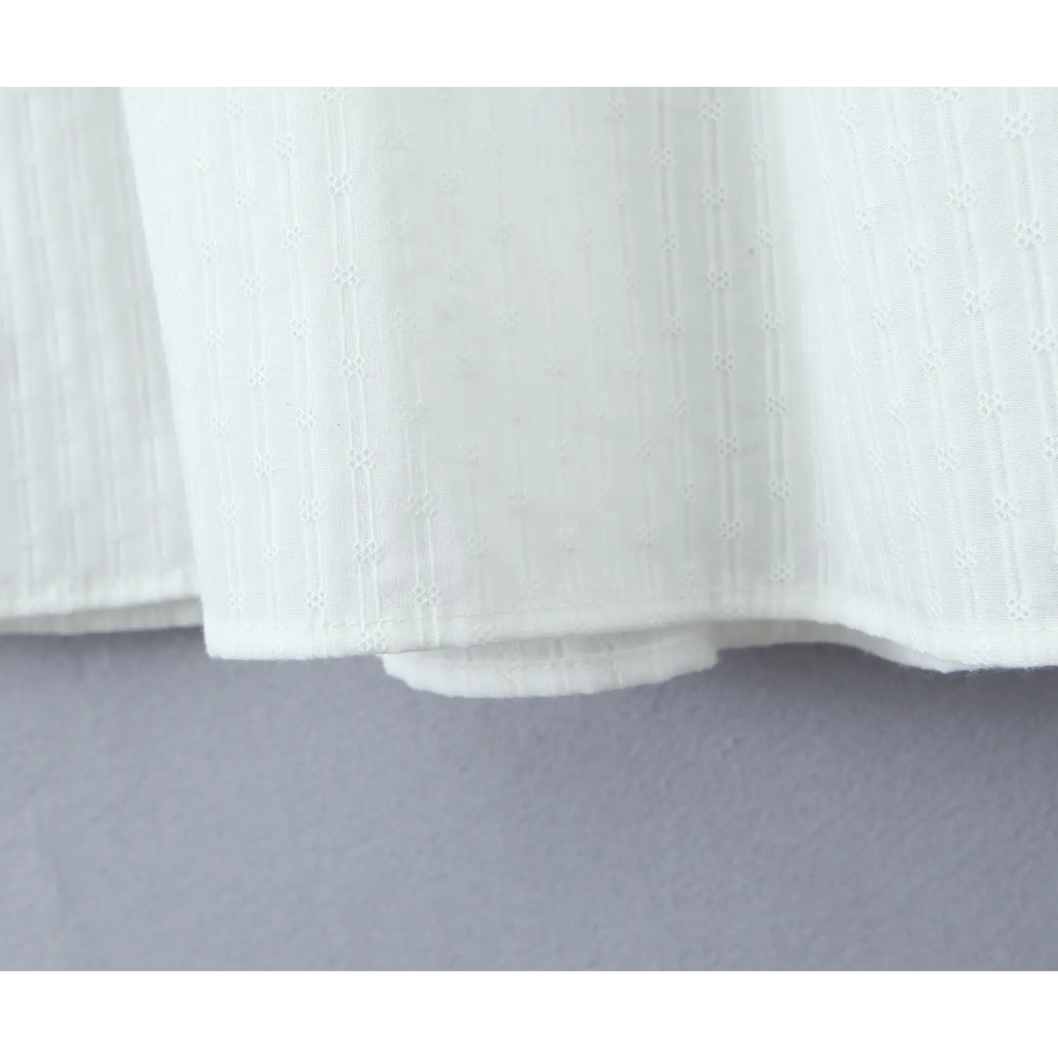 Close-up of the textured fabric and finished hem on a white tiered maxi skirt